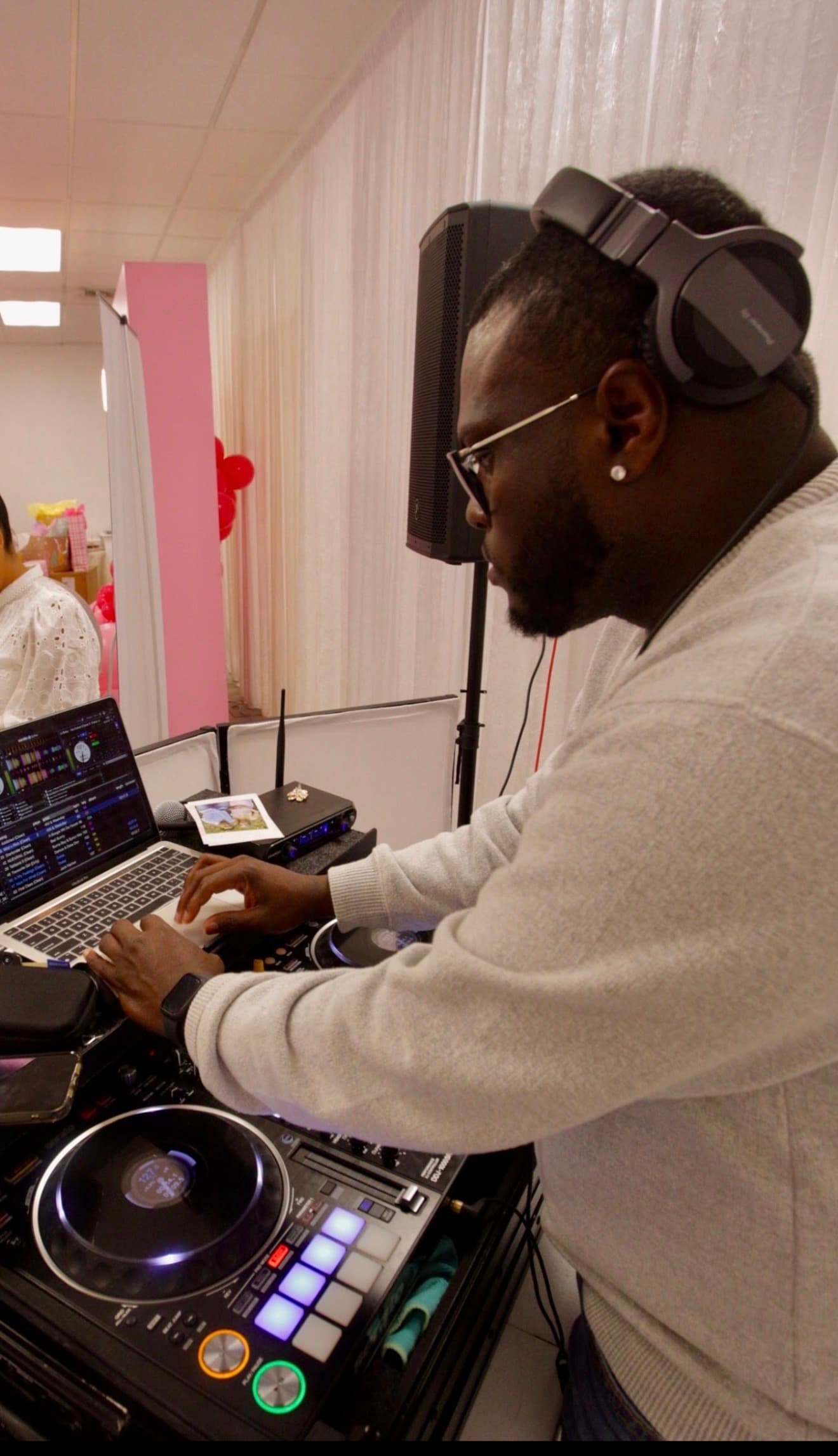 DJ wearing headphones and glasses mixes music on a laptop and controller at an event.