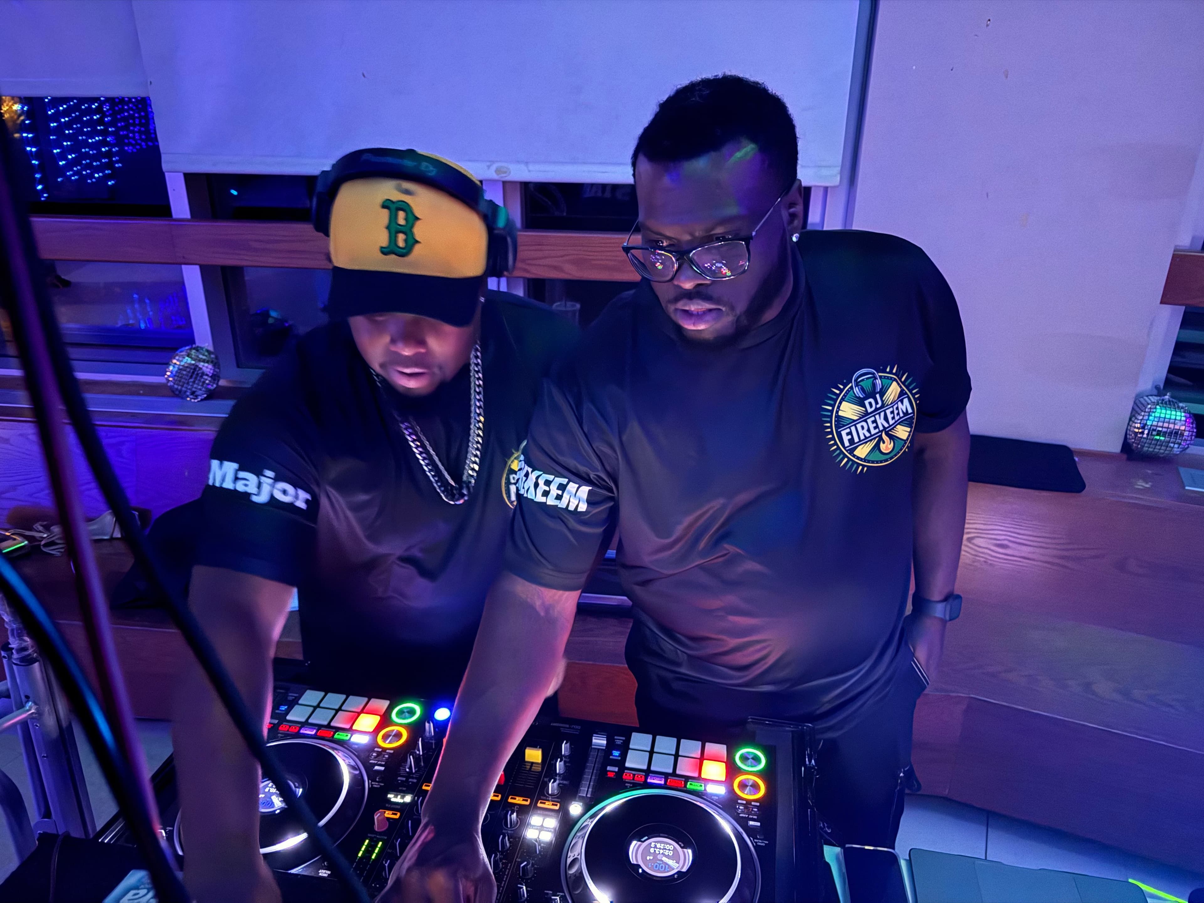 Two DJs operate a glowing mixing board under blue and purple ambient club lighting.