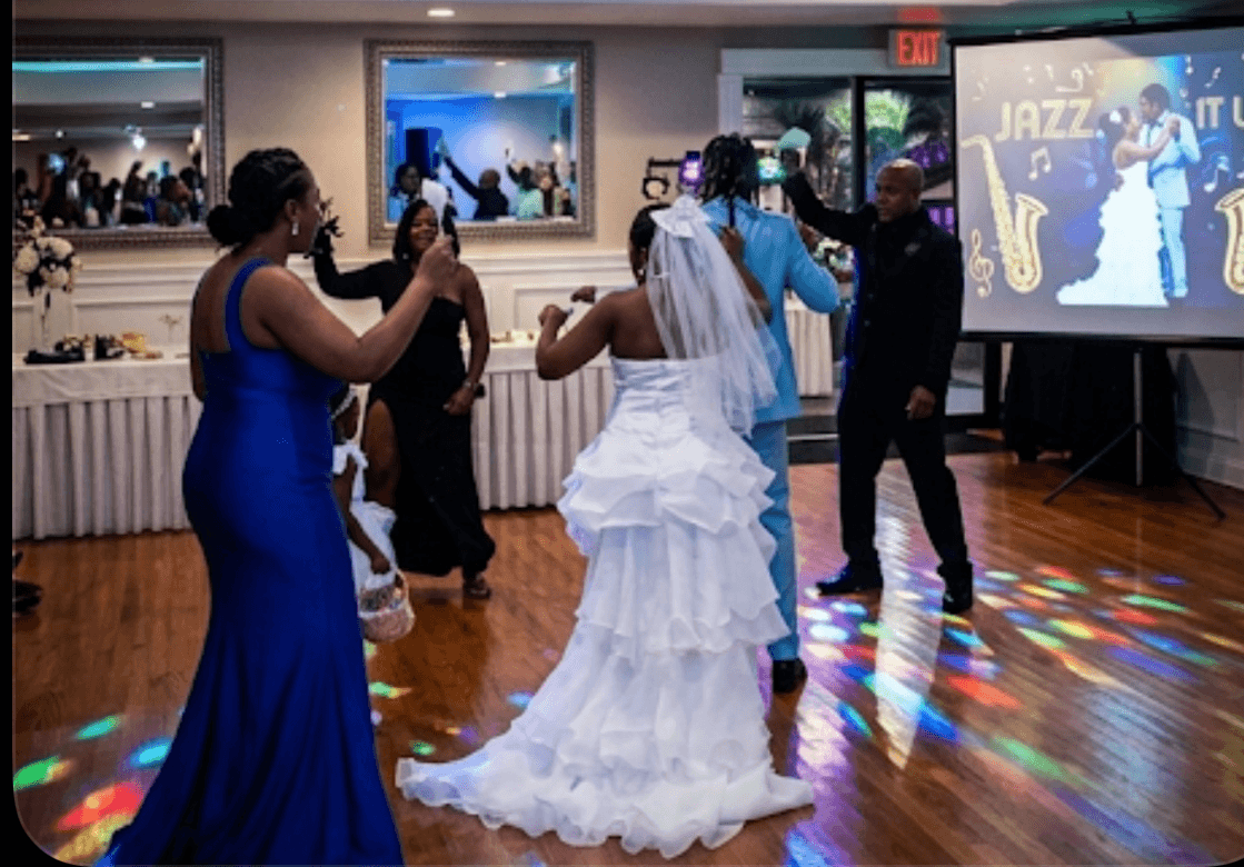 Bride and groom dance with guests on a wooden floor illuminated by colorful disco lights.